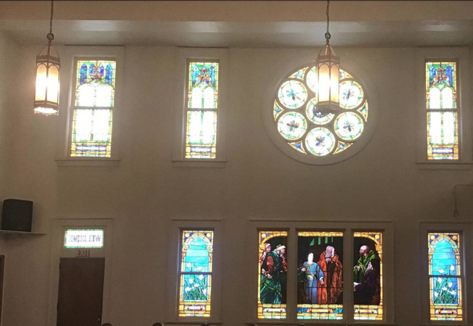 Interior sanctuary wall with tall stained glass windows and a rose window